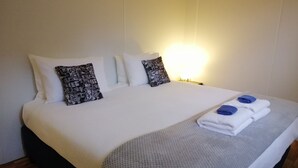 A neatly made bed with white bedding, two patterned pillows, and a folded towel with a blue accent. - Lucas Parklands - The Cube, peaceful getaway with direct access to 'Great Walk' (North Maleny)