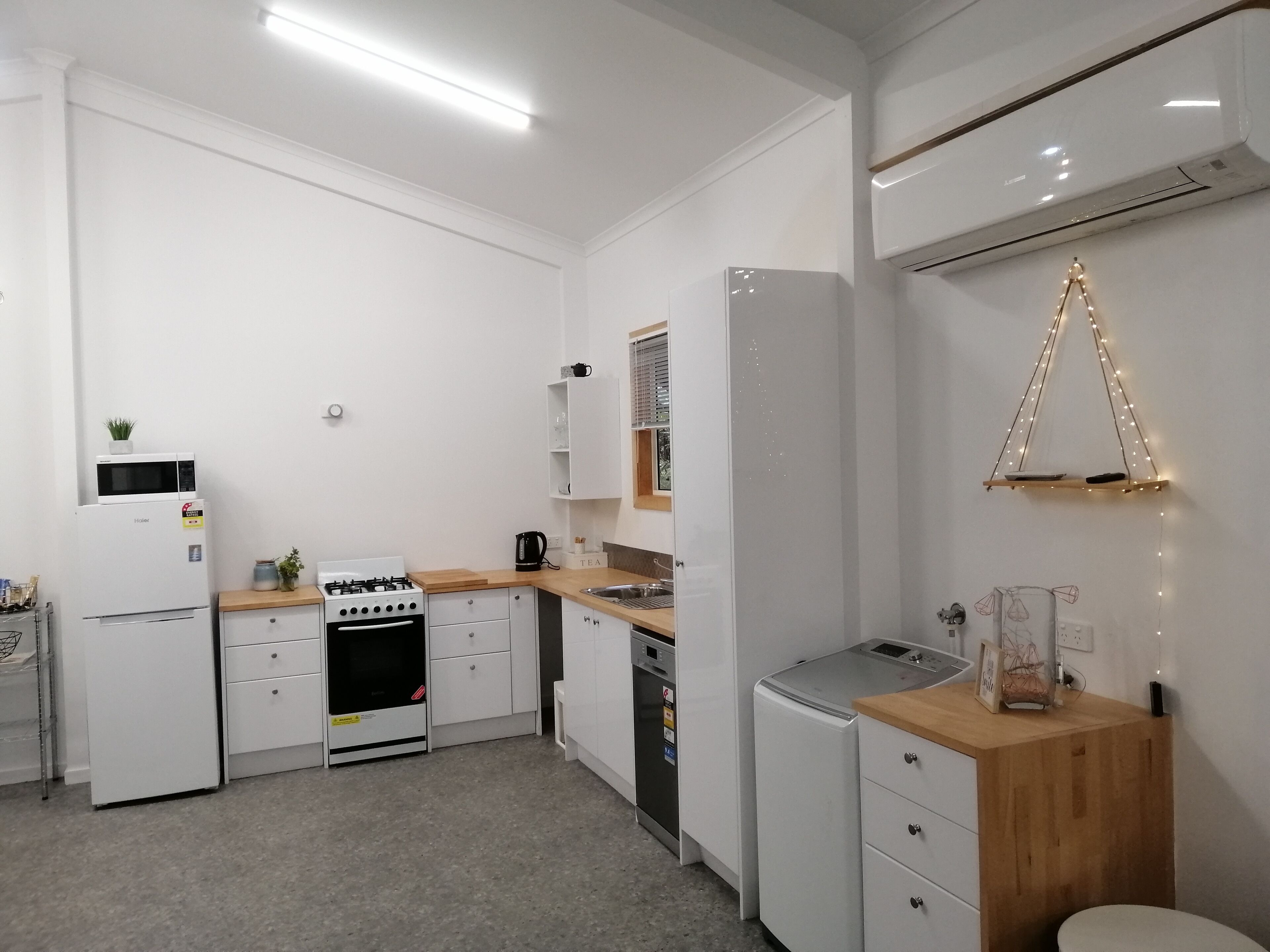 Eine kompakte Küche mit weißen Schränken, einem Einbauofen, einer Mikrowelle, einer Kaffeemaschine und einem kleinen Kühlschrank.