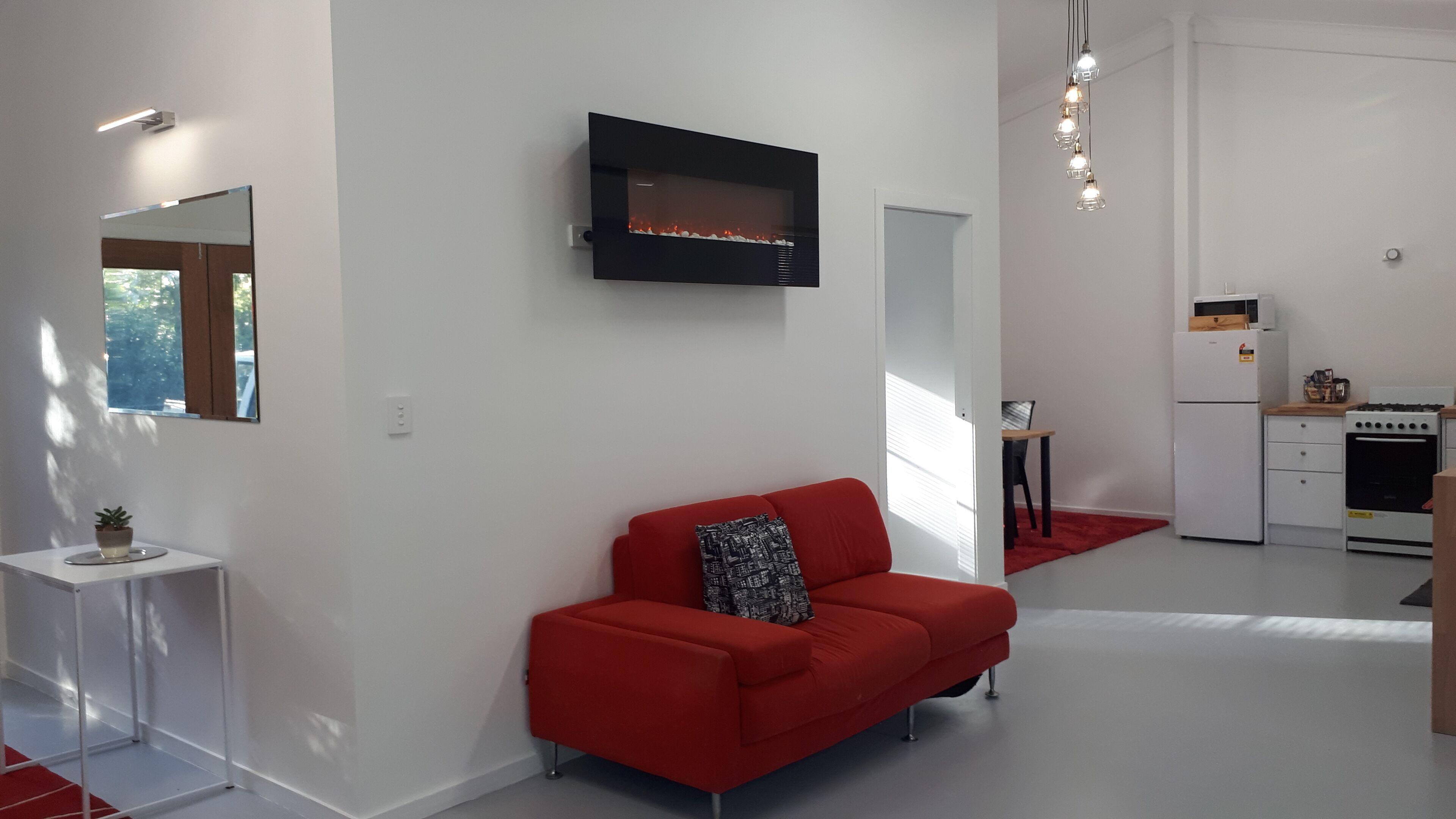 A modern living room with a red sofa, a black fireplace, and a kitchen area with white appliances.