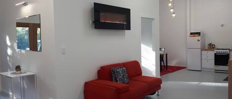 A modern living room with a red sofa, a black fireplace, and a kitchen area with white appliances.