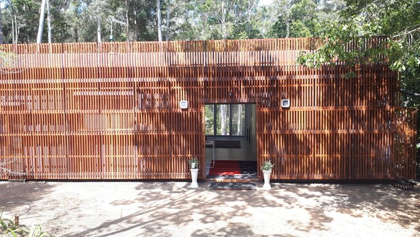 A modern building with a wooden facade, a large entrance, and a small garden area with potted plants. - Lucas Parklands - The Cube, peaceful getaway with direct access to 'Great Walk' (North Maleny)
