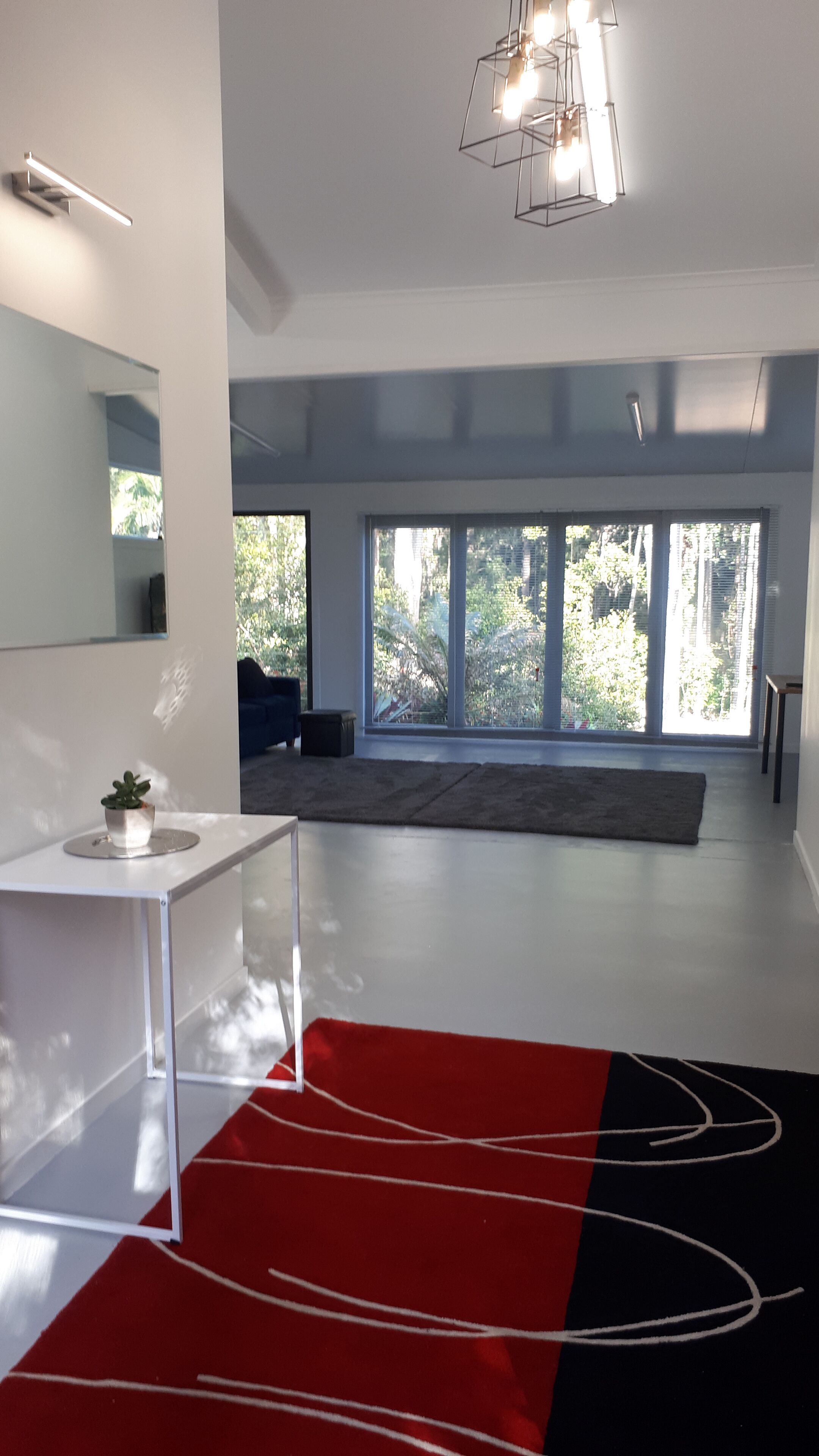 A modern room with a large window, a white desk, and a red and black rug.
