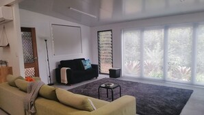 A modern living room with a green sofa, a black armchair, and a small table. - Lucas Parklands - The Cube, peaceful getaway with direct access to 'Great Walk' (North Maleny)