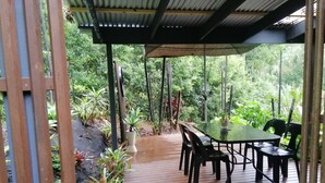 An outdoor patio with a table and chairs, surrounded by lush greenery and plants. - Lucas Parklands - The Cube, peaceful getaway with direct access to 'Great Walk' (North Maleny)