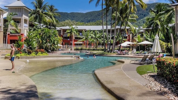 Een resort met een zwembad, palmbomen en een berg op de achtergrond.