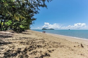 Une plage avec un ciel dégagé, une eau calme et des îles à l’horizon.