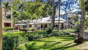 Een hotel met een overdekt terras, omringd door weelderige begroeiing en palmbomen.