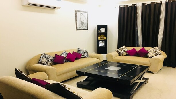 A living room with two beige sofas, a black coffee table, and a black cabinet with decorative items. - Moksha- Salvation (Gurugram)