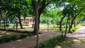A park with trees, a paved walkway, and a pavilion. - Moksha- Salvation (Gurugram)