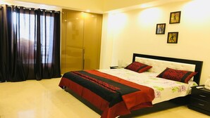 A bedroom with a bed, a nightstand, a bedside table, a wardrobe, and a window with curtains. - Moksha- Salvation (Gurugram)