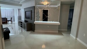 Una sala de estar moderna con un televisor de pantalla plana grande, una araña y un separador de vidrio.