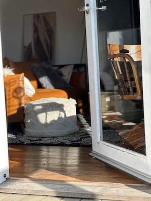 Una stanza con pavimento in legno, una coperta bianca lavorata a maglia, una sedia di legno e una porta vetrata che dà sull'esterno.