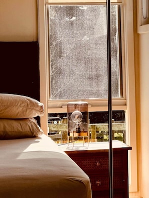 Una camera da letto con un'ampia finestra, un comodino con una lampada e un letto con cuscini.
