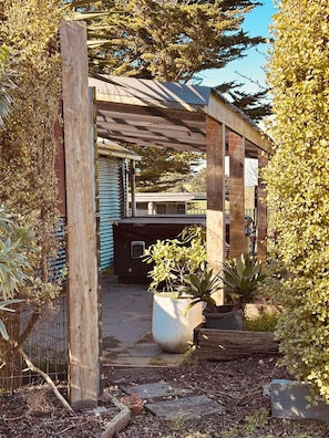 A covered outdoor area with a wooden structure, potted plants, and a pathway leading to a building.