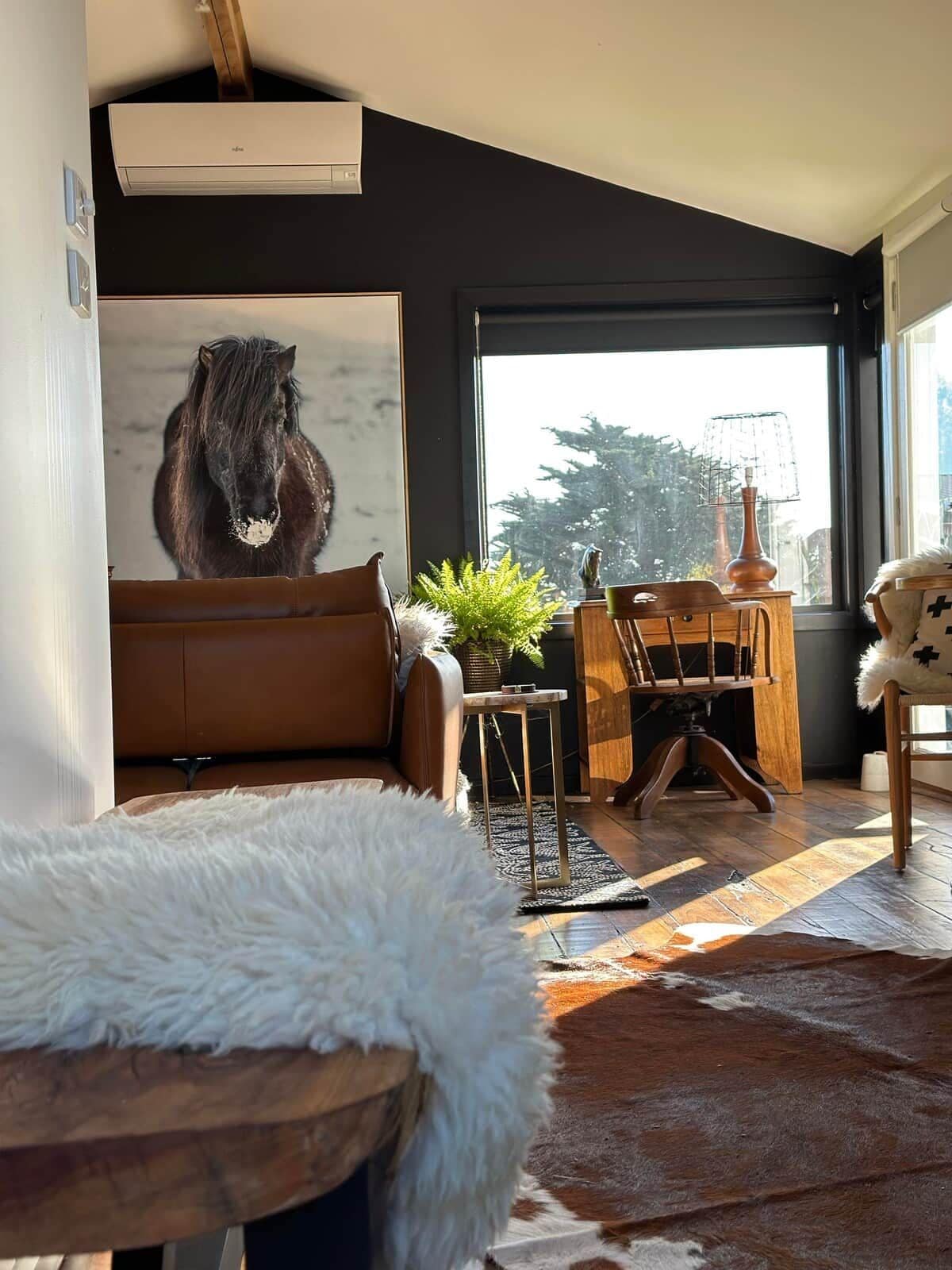 Una sala de estar moderna con un ventanal grande, un sofá de cuero marrón, una mesa de centro de madera y un plaid de piel.