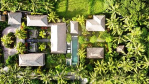 Ein Luftbild zeigt einen luxuriösen Urlaubsort mit Swimmingpool, mehreren Liegebereichen und üppiger tropischer Vegetation.