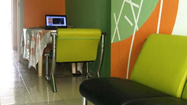 A dining area with a table and chairs, a laptop on the table, and a wall with a geometric design. - Morabeza Kriol Hostel (Praia)
