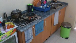 A kitchen with a gas stove, pots, a coffee maker, and a trash bin. - Morabeza Kriol Hostel (Praia)