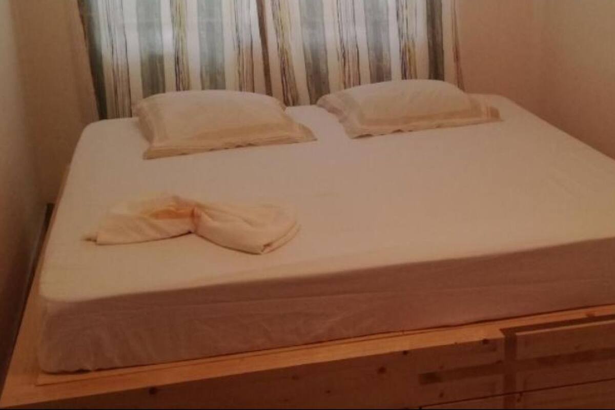 A single bed with a wooden headboard and drawers, a blanket, and pillows.