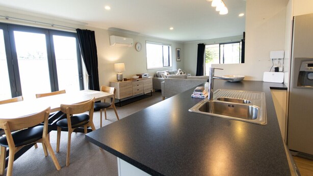 A modern kitchen with a central island, a dining area with chairs, and a sofa in the background.