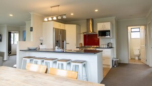 A modern kitchen with a central island, bar stools, a stainless steel range hood, and a microwave.