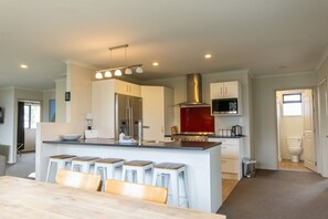 A modern kitchen with a central island, bar stools, a stainless steel range hood, and a microwave.