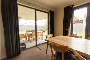 A room with a sliding glass door leading to an outdoor patio area, a wooden dining table with chairs, and a carpeted floor.