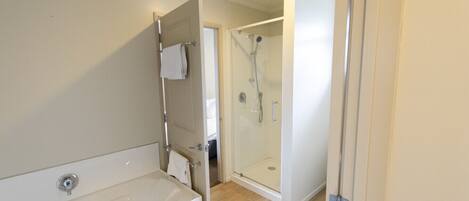 A bathroom with a bathtub, a shower enclosure, and a door leading to another room.