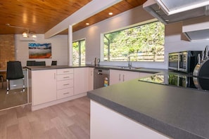 A modern kitchen with a large island, white cabinetry, and a view of greenery outside.