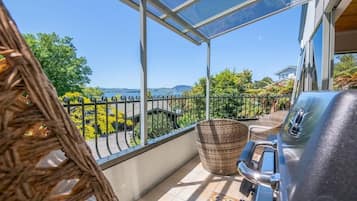 A balcony with a grill, wicker furniture, and a view of greenery and hills.
