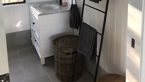Une petite salle de bain avec un meuble-lavabo blanc, un miroir, un porte-serviettes et un panier en osier.
