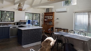 Une cuisine moderne dotée d’un îlot central, d’un coin repas avec une table et des chaises, et d’une grande fenêtre qui laisse entrer la lumière naturelle.