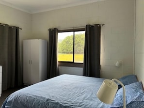A bedroom with a bed, a wardrobe, a window with curtains, and a view of greenery outside.