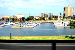 A marina with boats docked, buildings in the background, and a grassy area in the foreground.