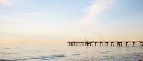 A pier extending into calm water with a clear sky.