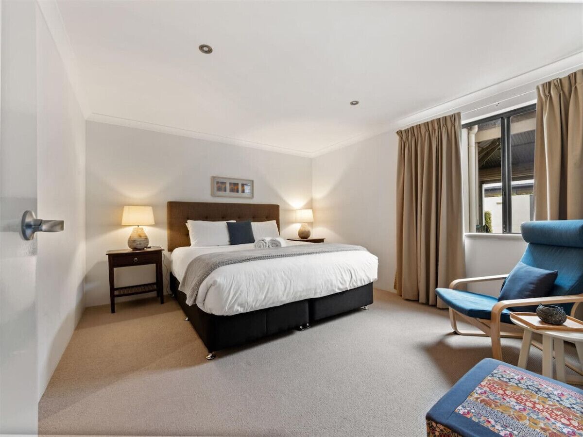A hotel room with a bed, bedside lamps, a chair, and a window with curtains.