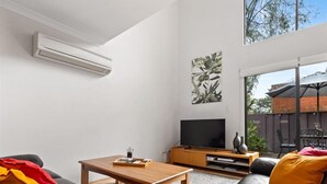 Un soggiorno moderno con televisione a schermo piatto, tavolino in legno, divani in pelle e una grande finestra con vista all'esterno.