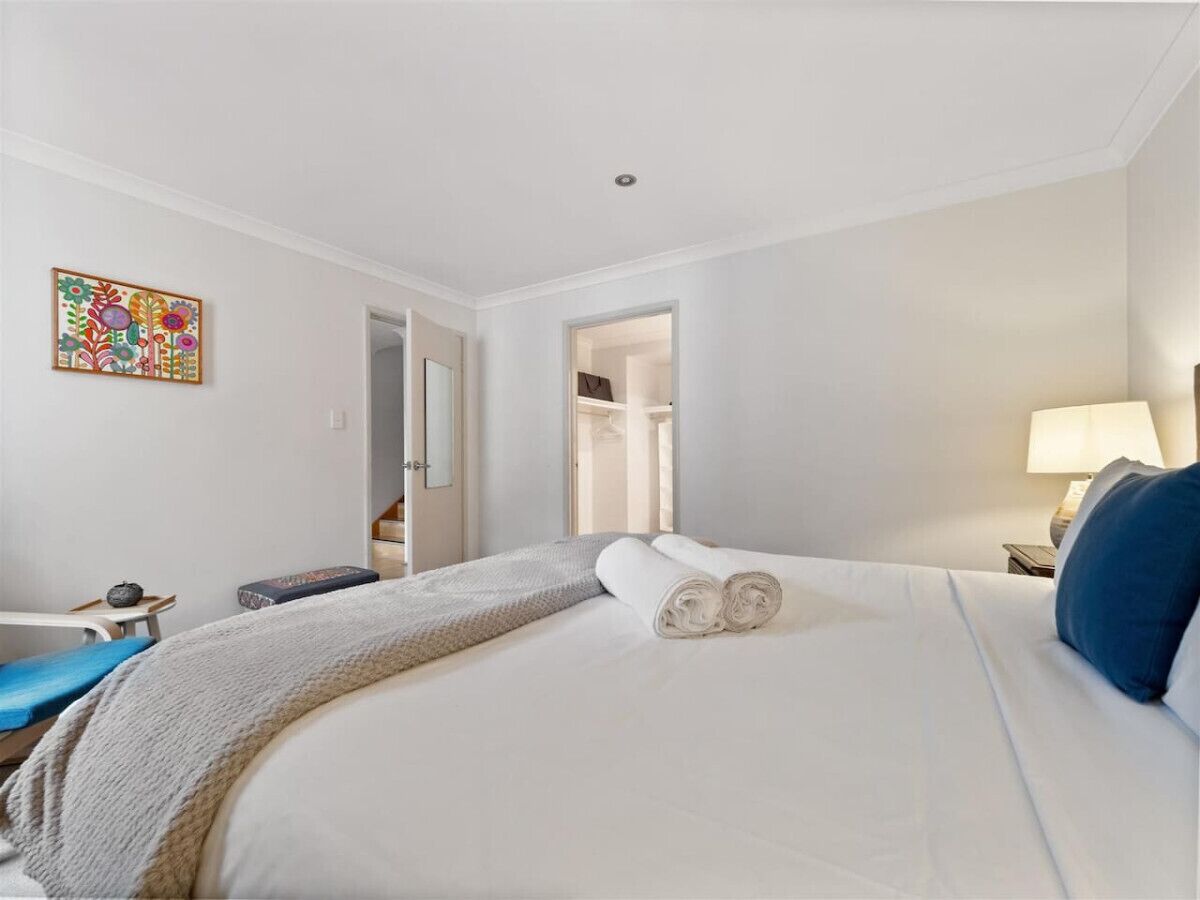 A hotel room with a bed, a nightstand, a lamp, a chair, and a door leading to a bathroom.