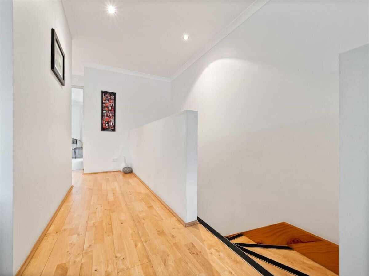 A hallway with wooden flooring, white walls, and a framed picture on the left.
