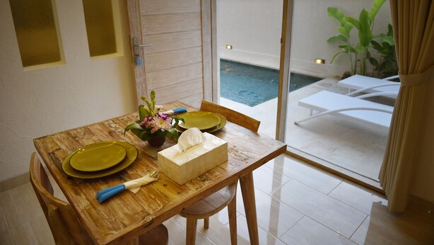 A dining table with green plates, a napkin, and a tissue box, set against a glass door leading to a pool area. - Green Studio Sanur (Bali)