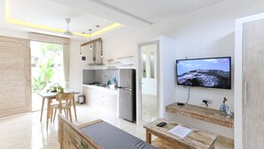 A modern kitchen with a flat-screen TV, wooden furniture, and a dining area with natural light. - Green Studio Sanur (Bali)