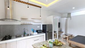 A modern kitchen with granite countertops, a stainless steel range hood, and a built-in microwave. There is a dining area with a wooden table and chairs, and a small wooden stool. - Green Studio Sanur (Bali)