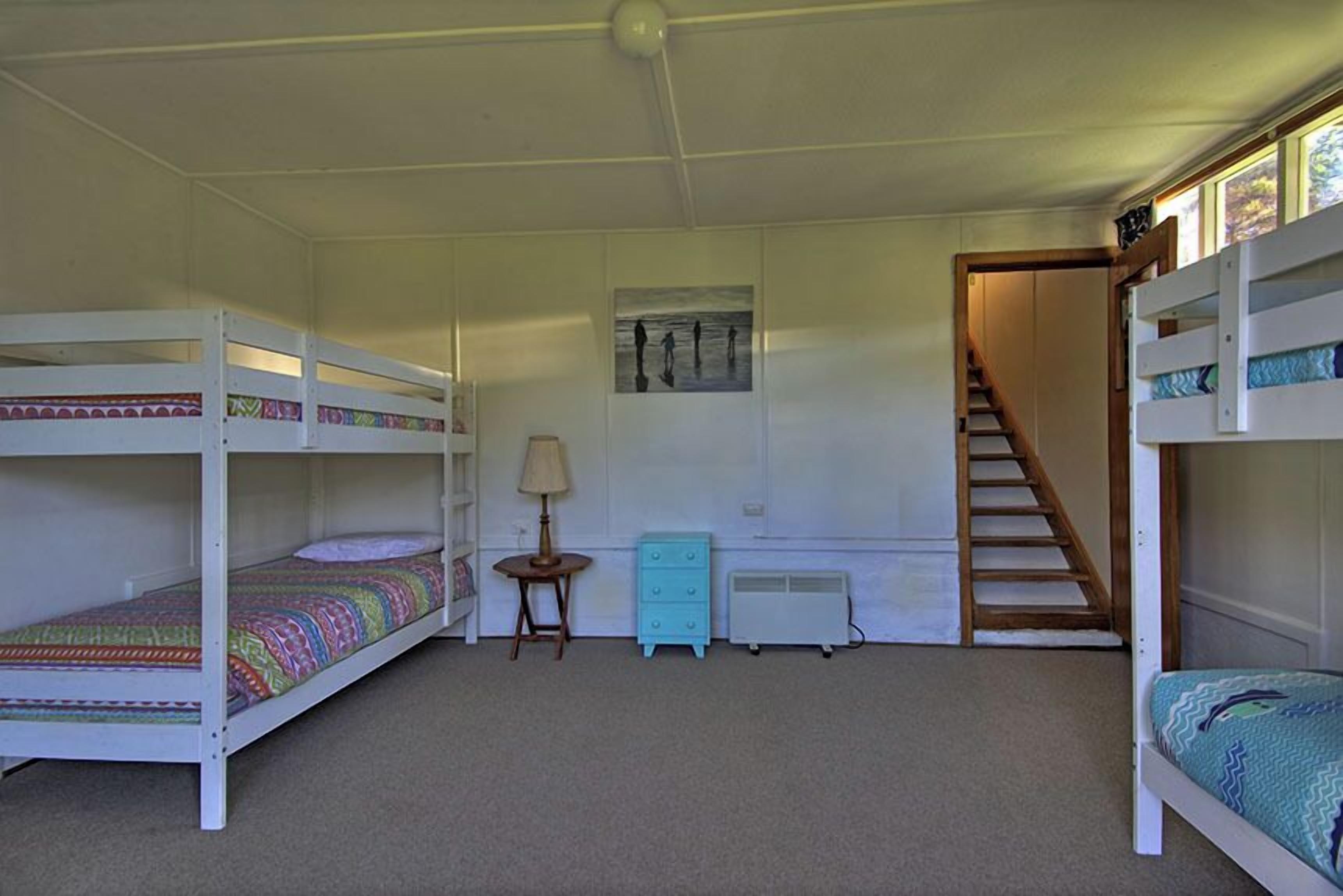 A room with bunk beds, a small table with a lamp, a dresser, and a radiator.