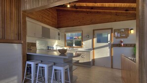 A modern kitchen with a central island, white bar stools, and wooden ceiling beams. - Freycinet Beachfront Retreat - Freycinet Holiday Houses (Coles Bay)