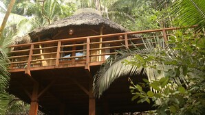 A wooden structure with a thatched roof, elevated on stilts, surrounded by dense tropical foliage. - Mint Cabin 1. Romantic Ecolodge in the jungle by the sea (San Pancho)