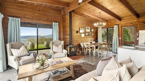 A cozy cabin interior with a fireplace, dining area, and large windows offering a scenic view.
