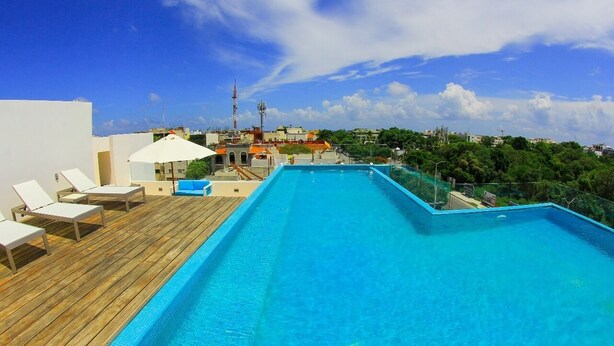A rooftop swimming pool with lounge chairs and umbrellas, surrounded by buildings and greenery. - Gris Coral st Calle 38 Condominium. Luxury one bedroom apartment next to beach. (Playa del Carmen)