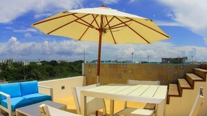 An outdoor patio with a table and chairs, a blue sofa, and a large umbrella. - Gris Coral st Calle 38 Condominium. Luxury one bedroom apartment next to beach. (Playa del Carmen)
