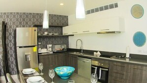 A modern kitchen with a central island, stainless steel appliances, and a dining area with a glass table and chairs. - Gris Coral st Calle 38 Condominium. Luxury one bedroom apartment next to beach. (Playa del Carmen)