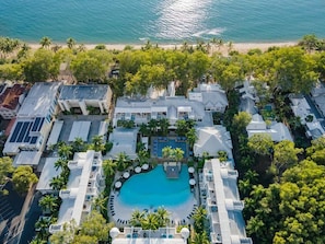 Una vista aerea di un resort con una piscina centrale, diversi edifici e una spiaggia.